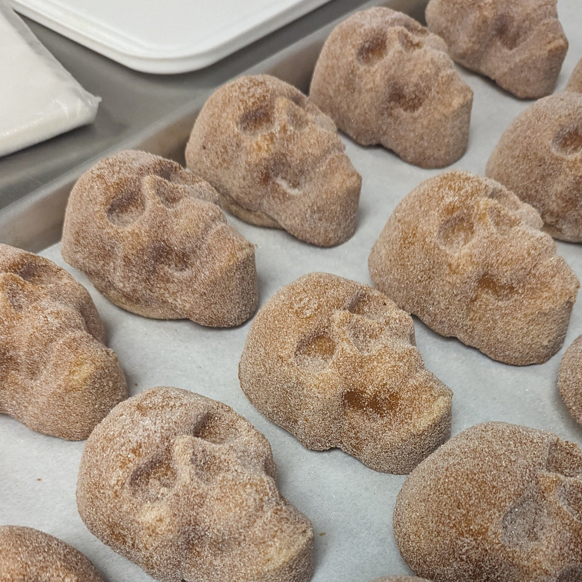 Sugar-coated skull-shaped pastries arranged on a parchment-lined baking tray.